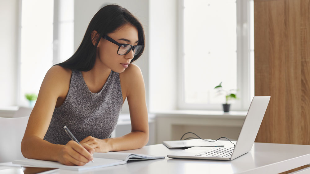 woman looking at a computer taking notes